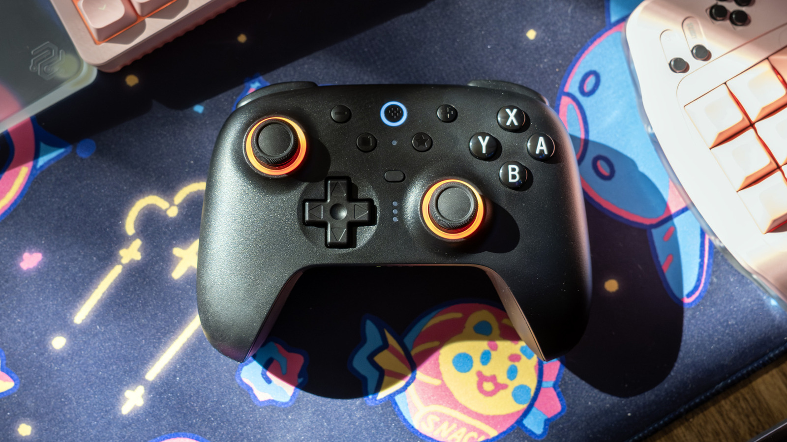 A 8BitDo volta à carga com o Ultimate 2, um controle sem fio que custa US$ 20 menos que o Switch 2 Pro da Nintendo e ainda entrega mais recursos que o modelo oficial. Analógicos TMR que resistem ao drift, gatilhos Hall effect, anéis de LED RGB, dois botões traseiros e uma base de carregamento dedicada vêm na caixa.

Nos testes, foram horas de Resident Evil Requiem, Hello Kitty Island Adventure e Mario Kart World sem nenhuma cãibra ou deslize, com elogios à ergonomia compacta e ao clique gostoso dos botões. A única crítica é um conjunto de botões pequenos e difíceis de ler de bate-pronto.

Por US$ 70, e muitas vezes menos em promoção, o Ultimate 2 prova que não é preciso pagar preço de topo de linha para ter desempenho de topo de linha. Aqui, o custo-benefício vence a lealdade à marca.